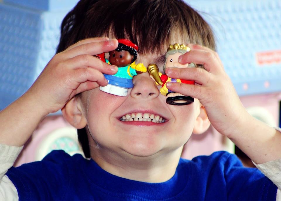 child holding toys over his eyes