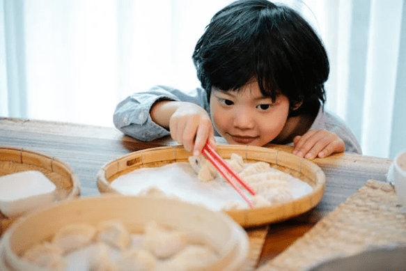 boy reaching for dumpling with red chopsticks